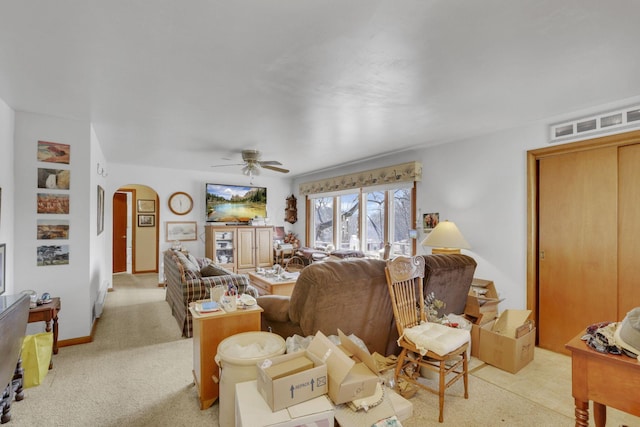 living area with arched walkways, light carpet, ceiling fan, and baseboards