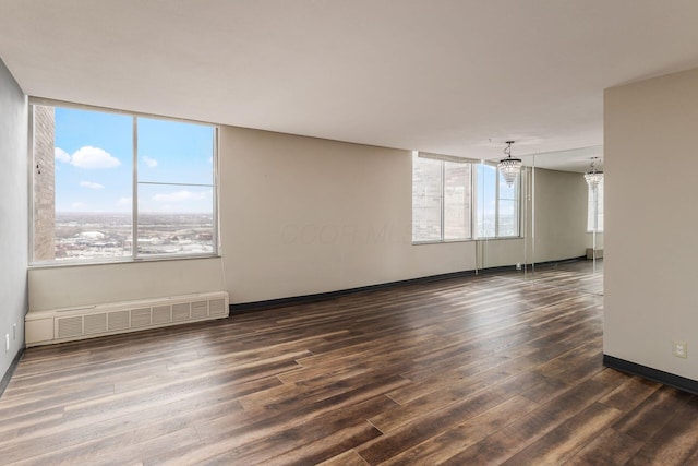 empty room with plenty of natural light, a notable chandelier, dark wood finished floors, and baseboards