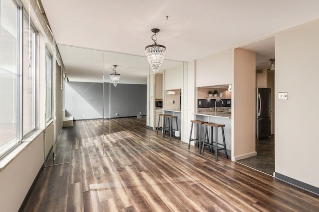 unfurnished living room with a sink, an inviting chandelier, baseboards, and wood finished floors