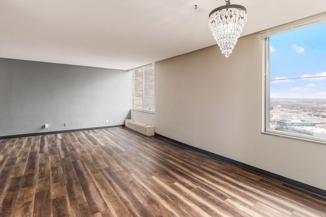 empty room with a chandelier, radiator heating unit, wood finished floors, and baseboards