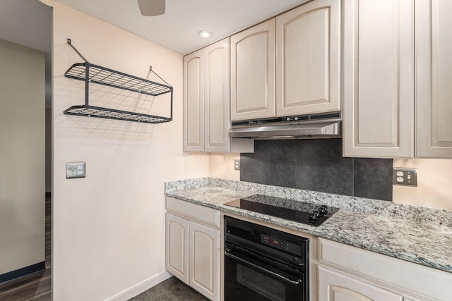 kitchen with cream cabinets, black appliances, light stone countertops, under cabinet range hood, and baseboards