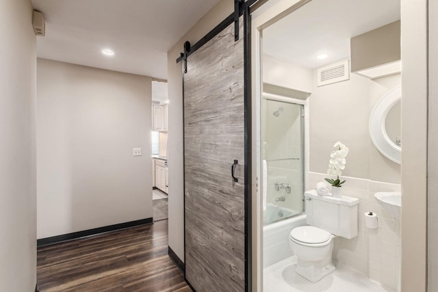 bathroom featuring visible vents, toilet, enclosed tub / shower combo, wood finished floors, and tile walls