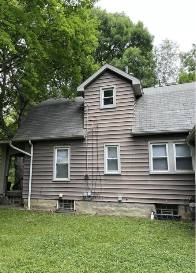 rear view of house with a lawn and roof with shingles