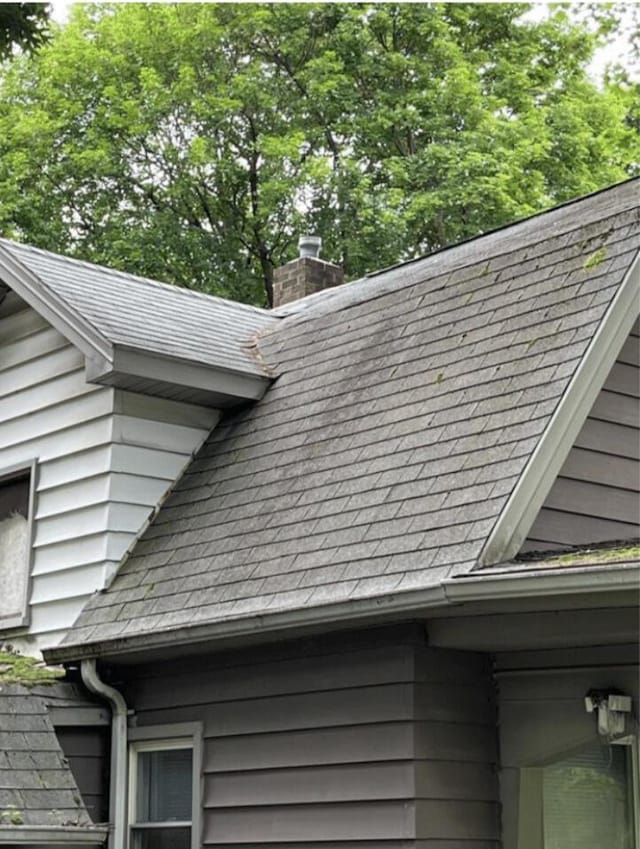 exterior details featuring gutters, a downspout, a chimney, and roof with shingles