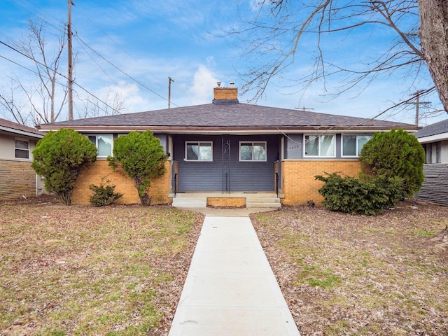 single story home with a chimney, a porch, and brick siding