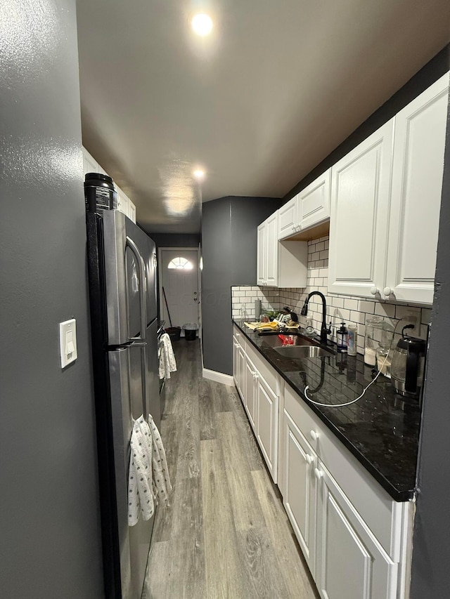 kitchen featuring light wood-style flooring, a sink, white cabinetry, freestanding refrigerator, and decorative backsplash