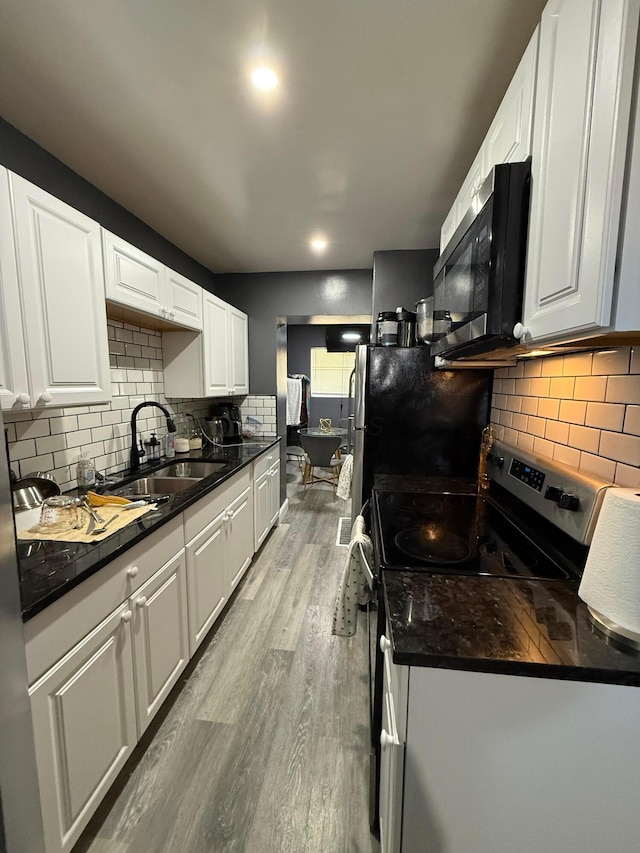 kitchen with a sink, white cabinetry, appliances with stainless steel finishes, light wood-type flooring, and decorative backsplash