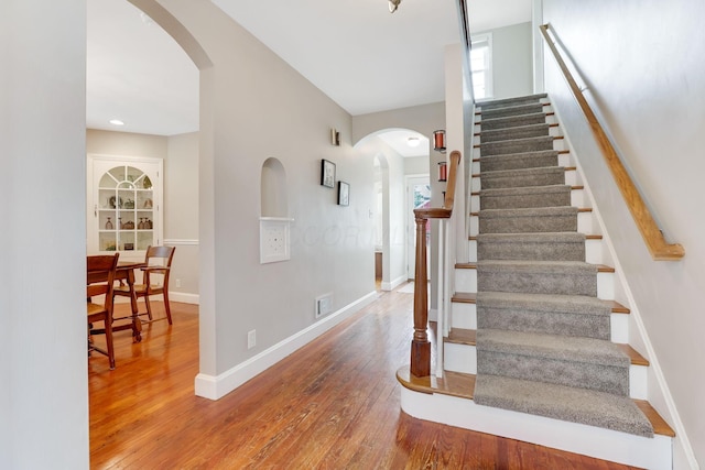 stairway featuring arched walkways, wood-type flooring, visible vents, and baseboards