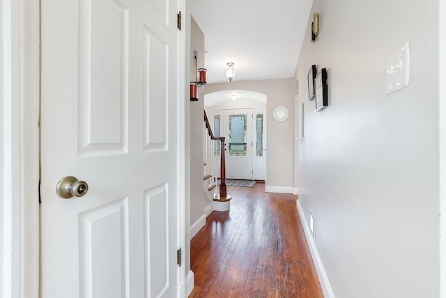 corridor featuring arched walkways, stairs, hardwood / wood-style flooring, and baseboards