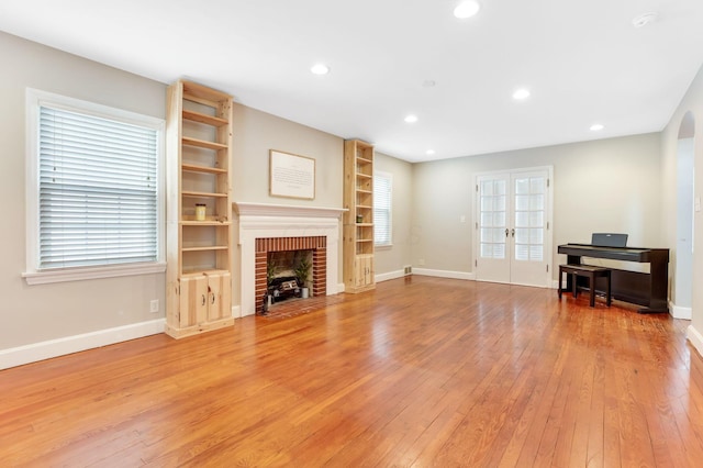 living area featuring a brick fireplace, baseboards, light wood-style flooring, and french doors