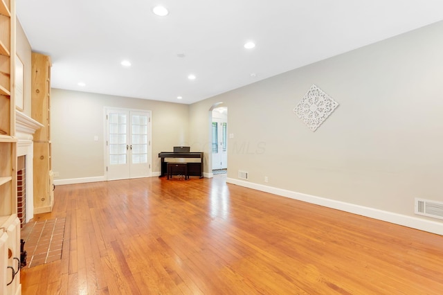 unfurnished living room with arched walkways, a fireplace, recessed lighting, visible vents, and light wood-type flooring