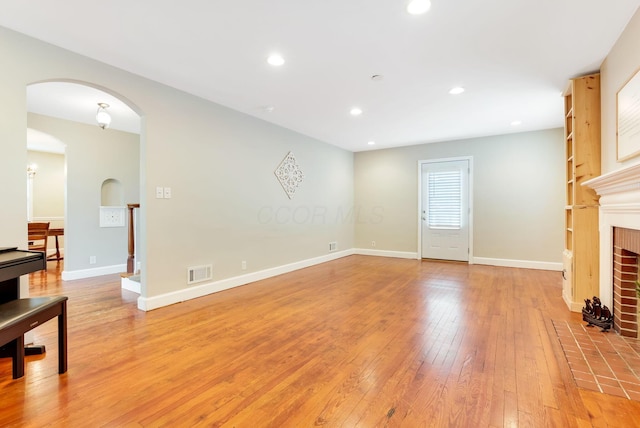 living area featuring visible vents, arched walkways, light wood-style flooring, a fireplace, and recessed lighting