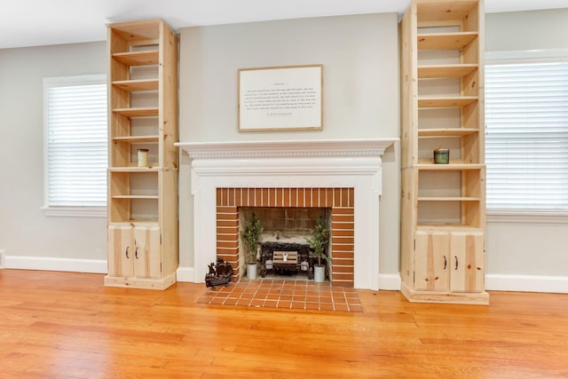 unfurnished living room with baseboards, a brick fireplace, and light wood-style floors