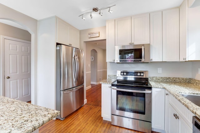 kitchen featuring arched walkways, light stone counters, light wood-style flooring, white cabinets, and appliances with stainless steel finishes