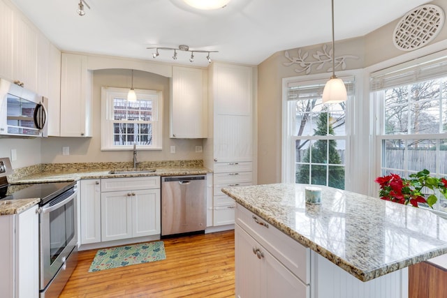 kitchen with white cabinets, appliances with stainless steel finishes, light wood-type flooring, pendant lighting, and a sink