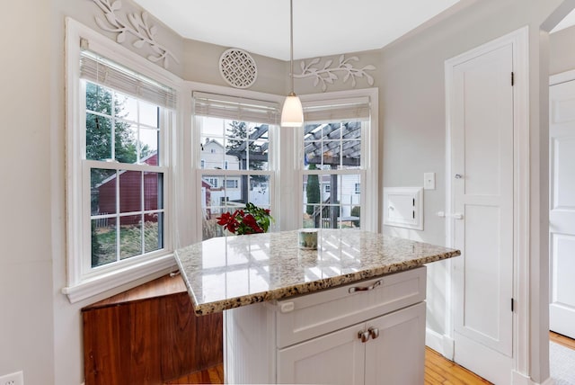 kitchen featuring a kitchen island, light stone counters, decorative light fixtures, light wood-type flooring, and white cabinetry