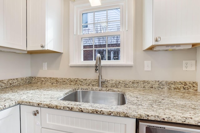 kitchen featuring light stone counters, white cabinetry, and a sink