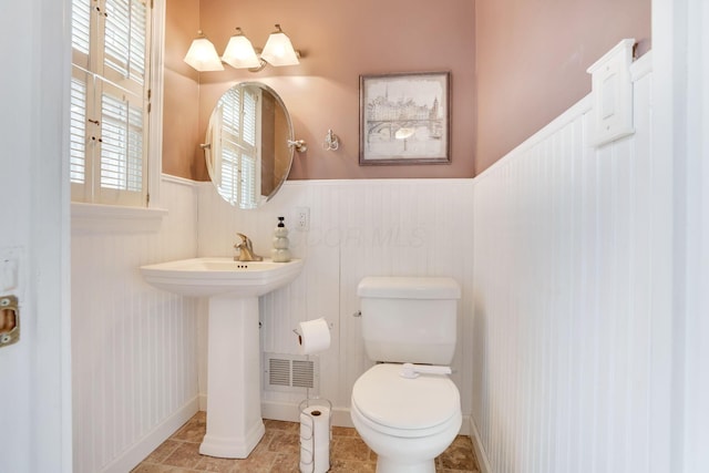 half bath featuring tile patterned flooring, wainscoting, visible vents, and toilet