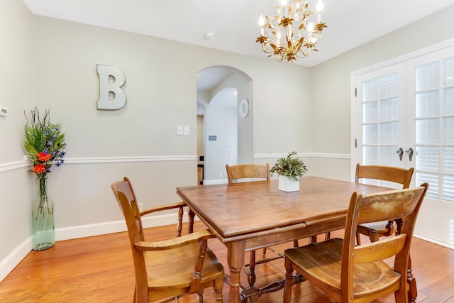 dining room with arched walkways, a chandelier, baseboards, french doors, and light wood finished floors