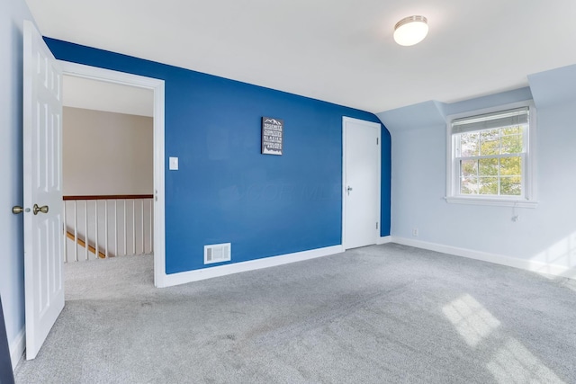 carpeted empty room with lofted ceiling, visible vents, and baseboards