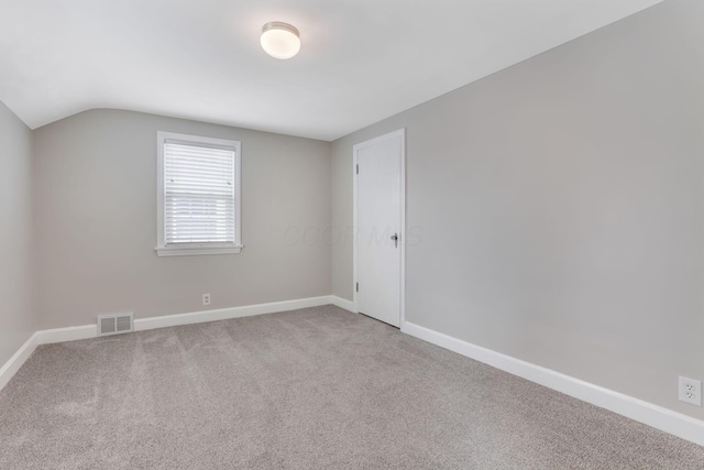 carpeted empty room featuring visible vents, vaulted ceiling, and baseboards