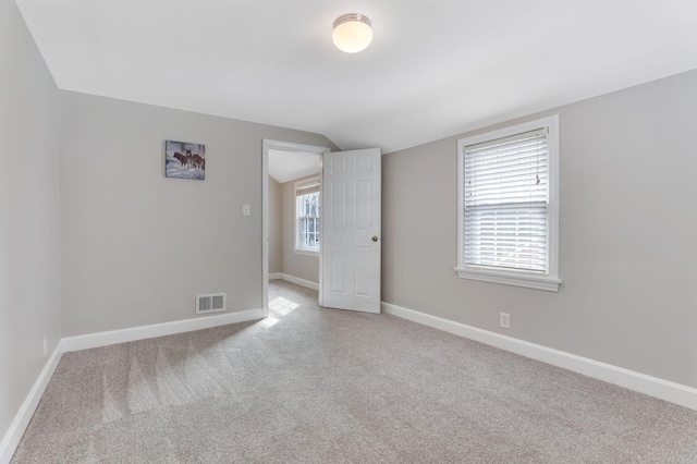 carpeted spare room featuring visible vents, vaulted ceiling, and baseboards