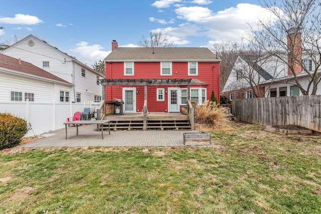 rear view of property featuring a fenced backyard, a yard, a wooden deck, a chimney, and a patio area