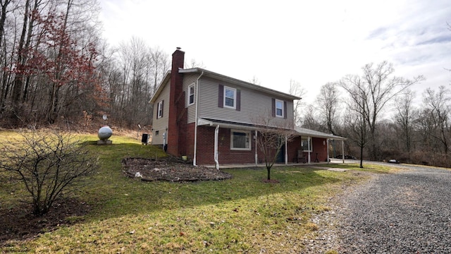 view of front of home featuring driveway, brick siding, a chimney, and a front lawn