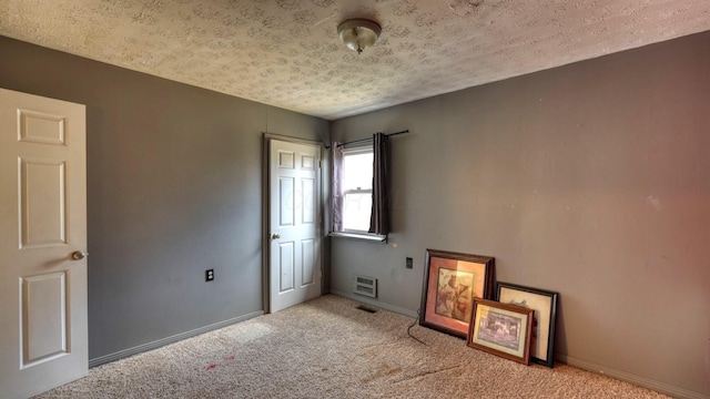 carpeted spare room with visible vents, a textured ceiling, and baseboards