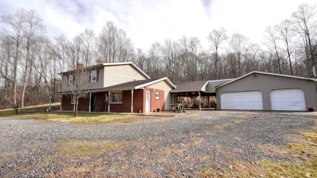 view of front of property featuring an attached garage, brick siding, gravel driveway, and a chimney