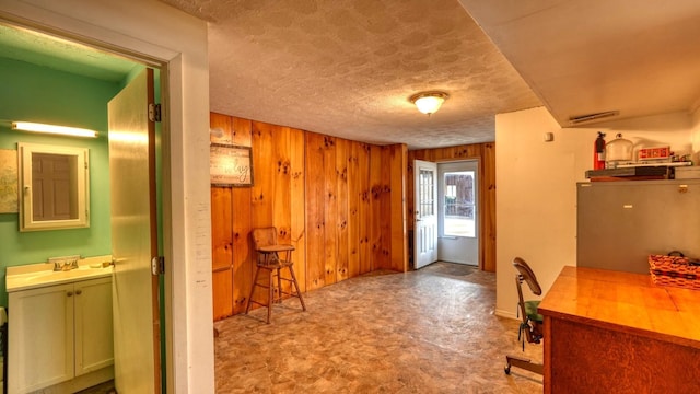 interior space featuring a textured ceiling, tile patterned floors, wooden walls, and a sink