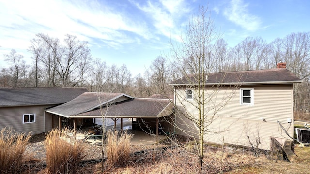 view of side of property with central air condition unit, a chimney, and a shingled roof