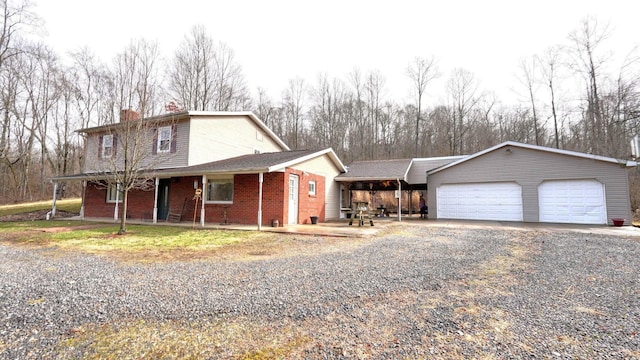 traditional-style home featuring brick siding, an attached garage, a chimney, and gravel driveway