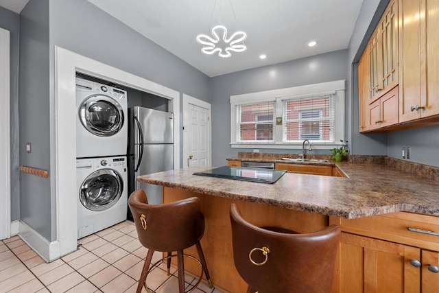 kitchen featuring stacked washer and dryer, light tile patterned floors, dark countertops, stainless steel appliances, and a sink