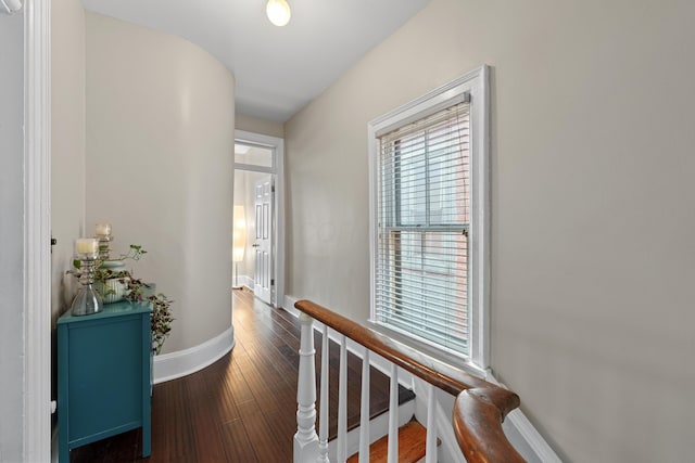 corridor with baseboards, wood finished floors, and an upstairs landing