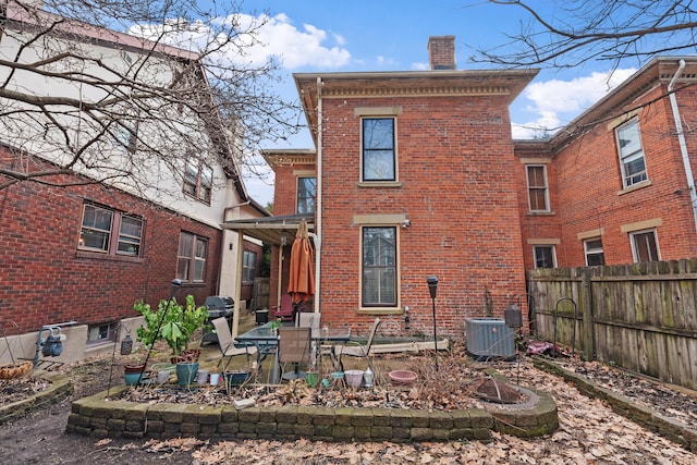 back of property with cooling unit, brick siding, fence, a chimney, and a patio area