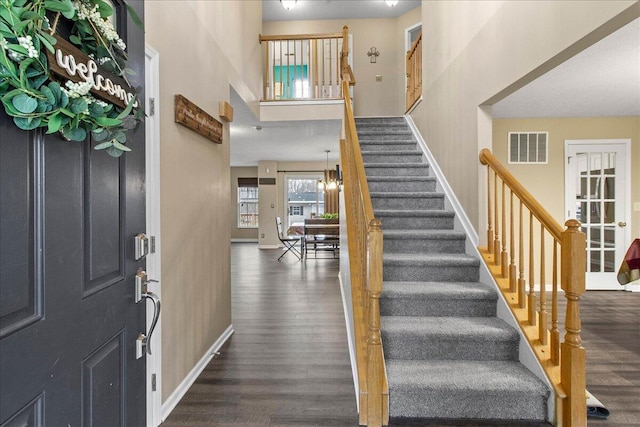 foyer entrance featuring dark wood-style flooring, visible vents, stairway, and baseboards