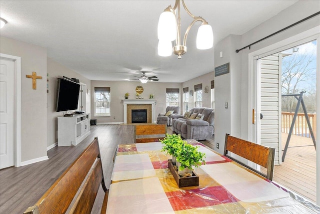 dining area featuring a fireplace with flush hearth, wood finished floors, baseboards, and ceiling fan with notable chandelier