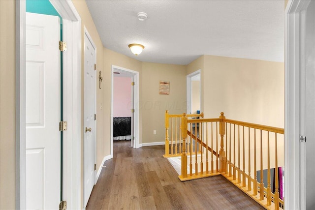 hallway with a textured ceiling, wood finished floors, an upstairs landing, and baseboards