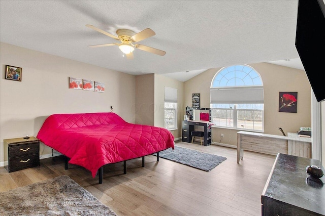 bedroom with ceiling fan, vaulted ceiling, a textured ceiling, and wood finished floors