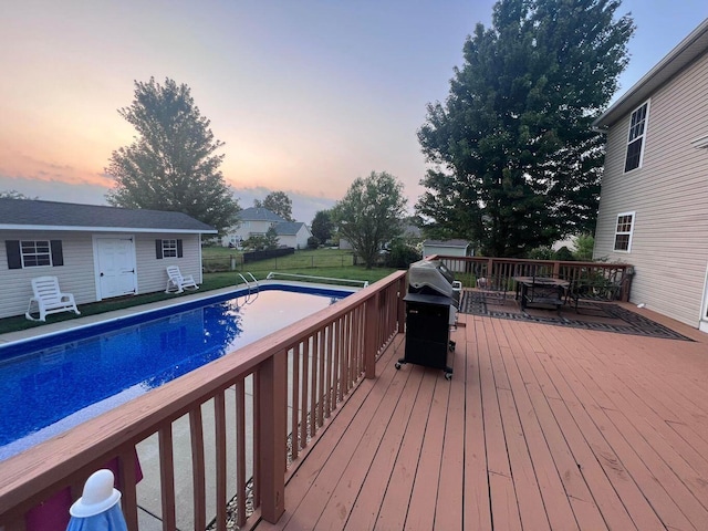 deck featuring an outdoor structure, area for grilling, fence, and a fenced in pool