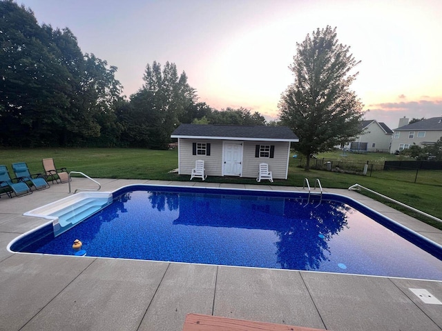 pool at dusk featuring an outbuilding, an outdoor pool, a lawn, and a patio