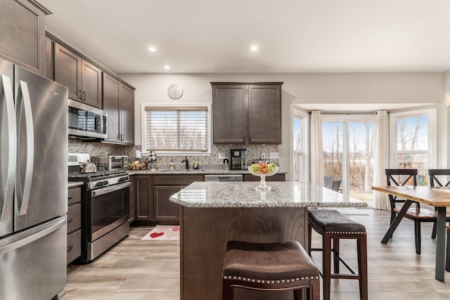 kitchen with appliances with stainless steel finishes, backsplash, dark brown cabinetry, and light stone countertops