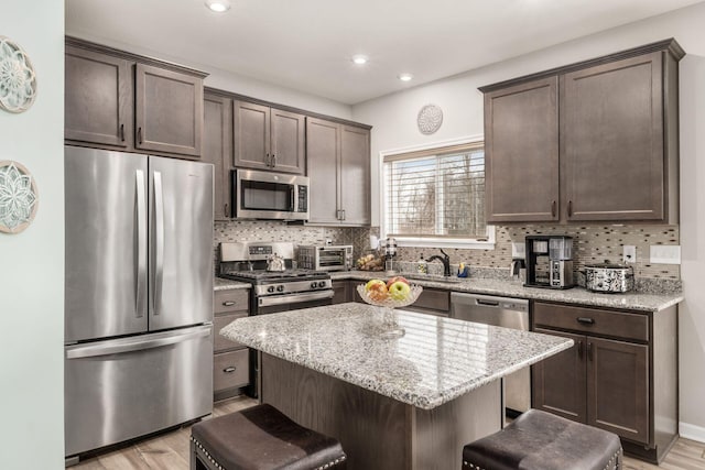 kitchen featuring dark brown cabinetry, tasteful backsplash, appliances with stainless steel finishes, and a breakfast bar area