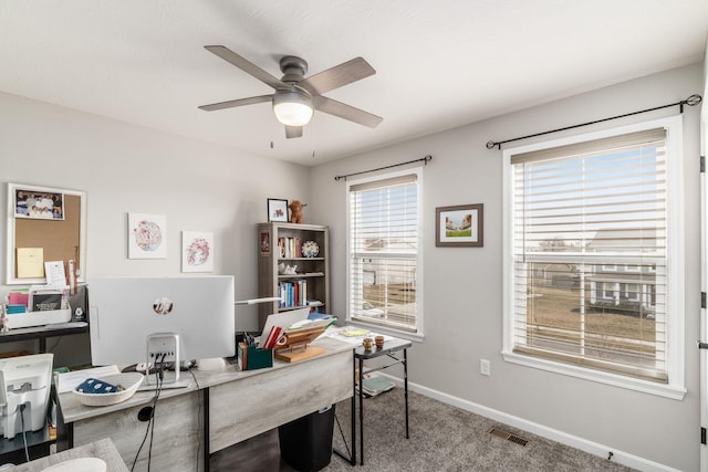 carpeted office space featuring a ceiling fan, a healthy amount of sunlight, visible vents, and baseboards