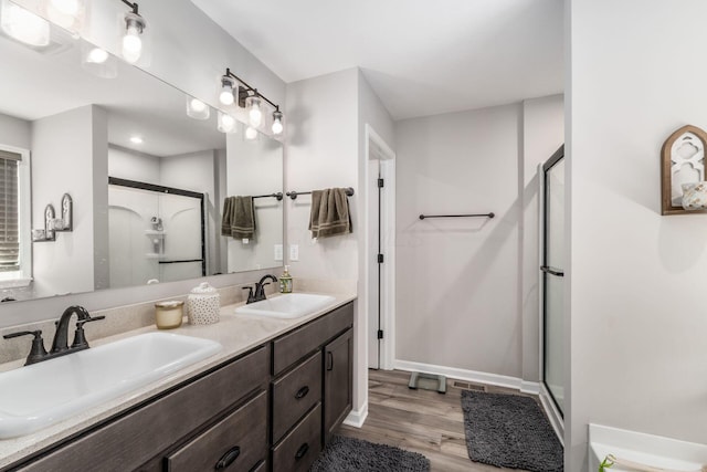 full bathroom with double vanity, wood finished floors, a stall shower, and a sink