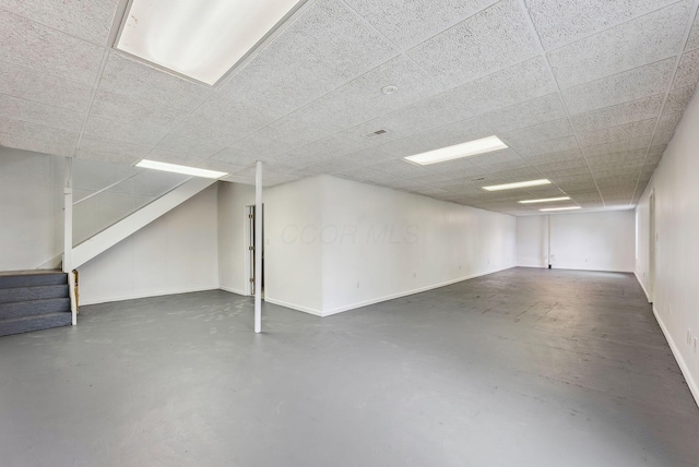 finished below grade area with a drop ceiling, stairway, and baseboards