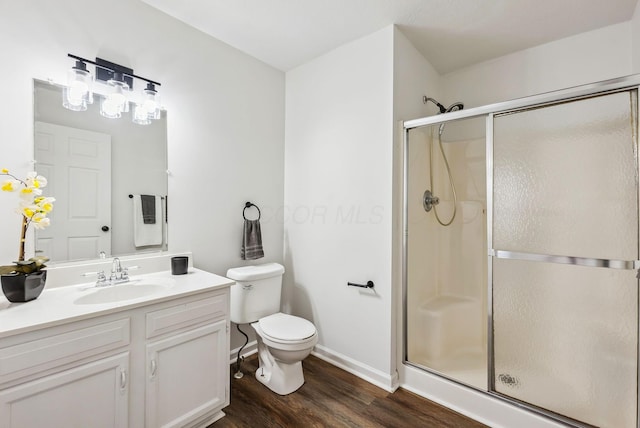 bathroom with toilet, vanity, a shower stall, wood finished floors, and baseboards