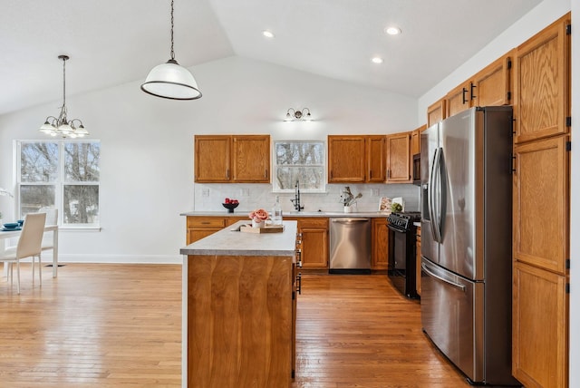 kitchen featuring appliances with stainless steel finishes, brown cabinetry, light wood-style floors, a healthy amount of sunlight, and a sink