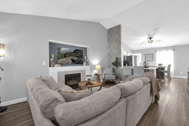 living room featuring vaulted ceiling, a glass covered fireplace, wood finished floors, and baseboards